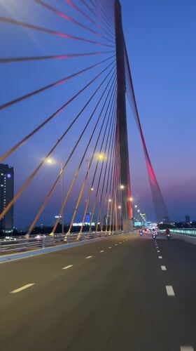 Vehicle crosses illuminated cable-stayed bridge at dusk in Da Nang