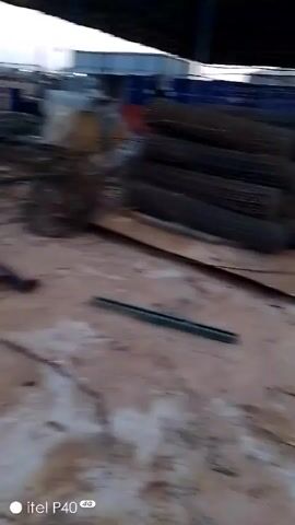The video shows an outdoor industrial site, likely a construction or storage area. The ground is a mix of dirt and debris. In the background, there are stacks of materials covered in tarps and what appears to be red containers. A cement mixer, painted yellow and blue, is visible. The camera moves quickly, making it difficult to discern specific details. The video is somewhat blurry and has a low resolution. The watermark "itel P40" is present in the corner of the screen.