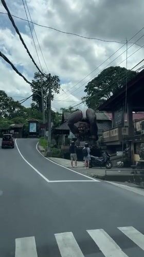 Vehicle stops at pedestrian crossing near statue in Tegallalang, Bali