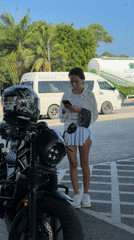 Woman checks phone beside motorcycle in Thailand