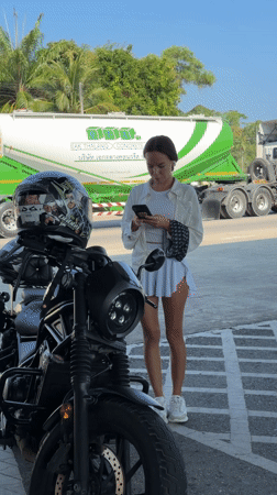 Woman checks phone beside motorcycle in Thailand