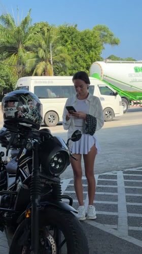 Woman checks phone beside motorcycle in Thailand