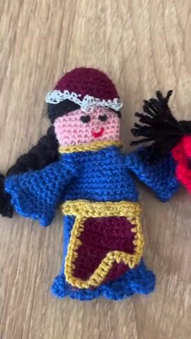 A video shows a close-up view of several crocheted dolls displayed on a wooden surface. The dolls are small and appear to be finger puppets or small decorative figures. They are dressed in various colorful outfits, featuring traditional or folk-inspired designs. Each doll has a crocheted face with embroidered features like eyes, nose, and mouth. The dolls are positioned next to each other, allowing for a clear view of their intricate details and craftsmanship. The lighting suggests an indoor setting, possibly a tabletop or a shelf. The video pans across the dolls, showcasing their diverse styles and colors.