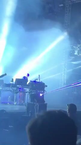 The video shows a person playing a keyboard on a stage. There are colorful lights and smoke in the background. Another person is seen dancing in front of the keyboard player. The scene appears to be a concert or live music performance.