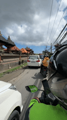 Motorcyclist navigates congested Balinese street amid traditional architecture