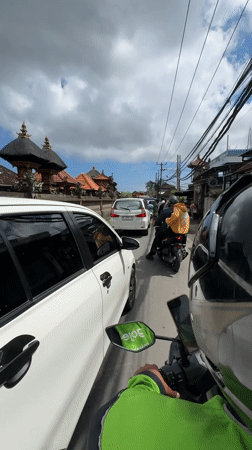 Motorcyclist navigates congested Balinese street amid traditional architecture
