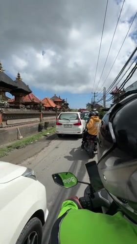 Motorcyclist navigates congested Balinese street amid traditional architecture
