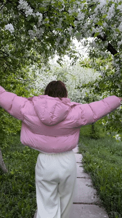 Woman walks blooming tree-lined pathway in Druzhino, Russia