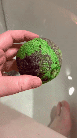 Green bath bomb dissolves into a candlelit tub in Hrodna