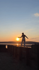 Woman reaches toward sunset at water's edge in Chaikovsky
