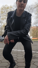 Woman in black leather jacket crouches on pavement