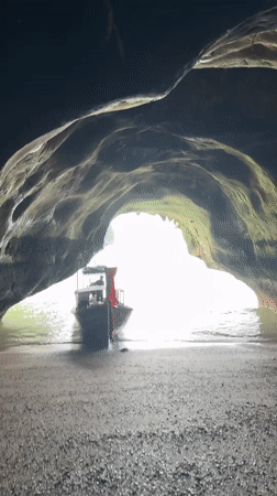 Cave mouth frames a red-canopied boat on Thai waters