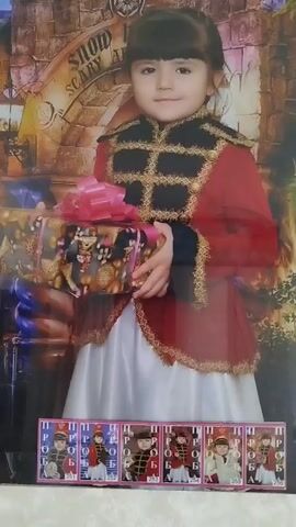 The video displays a series of photographs. The first photograph shows a young girl in a red and gold costume, holding a gift. Below this photo are six smaller, identical images of the same girl. The second photograph, which is blurred at the beginning, shows a boy and a woman smiling. As the video progresses, the image comes into focus, clearly showing the boy and woman. The third photograph shows a man and a young girl with pigtails. The overall impression is a collection of posed family portraits.