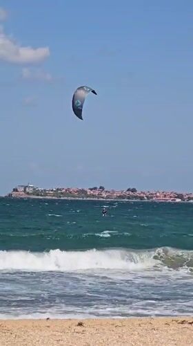 Kitesurfers ride choppy coastal waters near a beachside town.
