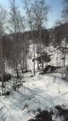 The video shows a snowy landscape with trees and a ski lift. The view appears to be from inside the ski lift as it travels upwards. A metal tower is visible in the snow-covered landscape. A person wearing a ski helmet and gloves can be seen in the foreground.