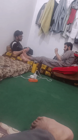 Two men converse on floor mattresses in Peshawar room