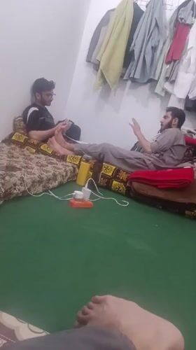 Two men converse on floor mattresses in Peshawar room