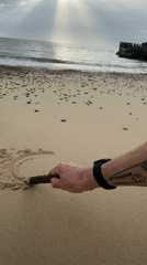 Person draws in sand at East Suffolk beach