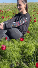 Woman sits smiling in red flower field near Rodniki