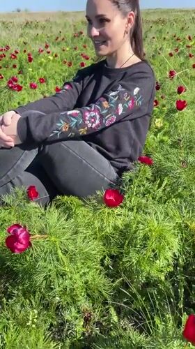 Woman sits smiling in red flower field near Rodniki