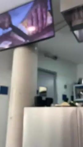 The video shows a stainless steel counter with a blue logo that reads “Le Cordon Bleu, Paris, 1895”. In the background, a chef in a white uniform and tall white hat prepares food on a stainless steel counter. There are various containers and utensils on the counter. A TV screen is visible in the upper left corner, showing a close-up of hands cutting food. The environment appears to be a commercial kitchen.
