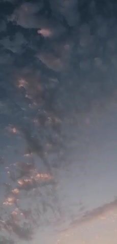 The video shows a cloudy sky at dusk. The clouds are a mix of dark blues and grays, with some hints of pink and orange from the setting sun. The camera is angled upwards, capturing the vast expanse of the sky. There are no people or objects visible in the frame. The environment appears to be outdoors, with no indication of any specific location. The video is silent, with no sound effects or music.