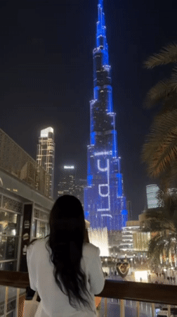 Woman views illuminated Burj Khalifa from Dubai balcony