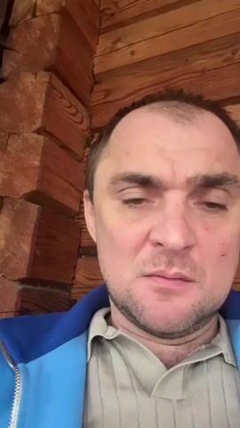 A man with short brown hair and a beard, wearing a blue jacket over a beige shirt, is facing the camera. He appears somewhat disheveled and possibly intoxicated. There's a small cut or mark on his left cheek. The background consists of wooden paneling. He says, "Pizdets, сижу бухой нахуй" which translates to "Damn, I'm sitting drunk as fuck" and then adds "Но вроде все нормально" or "But everything seems okay."