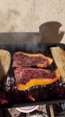 Backyard barbecue grills steaks and bread with visible smoke