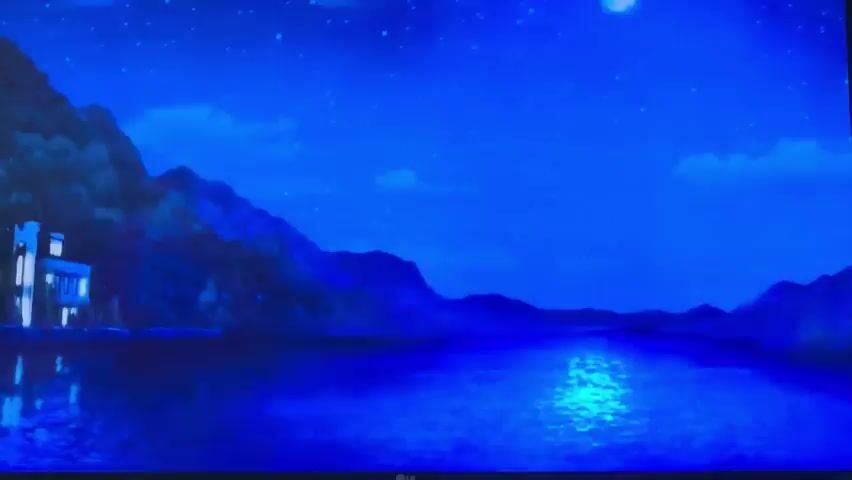 The video opens with a wide shot of a serene lake reflecting a moonlit night sky. Mountains loom in the background, with a large, illuminated building on the left shore. The scene then transitions to a closer view of the building, which appears to be a stately manor or castle, with many windows lit from within. Several horse-drawn carriages are parked in front of the building. A group of people, dressed in formal attire, are gathered near the entrance. The atmosphere is calm and mysterious.