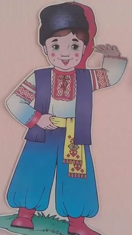The video shows a decorated wall with two cutouts of children in traditional Ukrainian clothing. To the left is a boy wearing a black hat, a white embroidered shirt, a blue vest, blue pants, and red boots. He has rosy cheeks and a friendly smile. To the right is a girl wearing a flower wreath with ribbons, a white embroidered shirt, a red belt, a checkered skirt, and red boots. She also has rosy cheeks and a smile, with her hands on her hips. Between the cutouts, on the wall, is a rectangular sign with different colored bars, each containing text in Ukrainian. The text appears to be various greetings such as "Good morning!", "Good afternoon!", "Good evening!", and "Greetings!". There are also some colorful curved lines emanating from a central oval on the left side of the sign, with the text "Ukrainian language" partially visible within the oval. The background is a pale pink wall, and the bottom of the cutouts show a hint of green grass. The lighting is consistent and seems to be indoors.