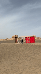Two visitors approach decorative sign in Dunhuang desert