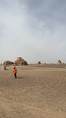 Two visitors approach decorative sign in Dunhuang desert