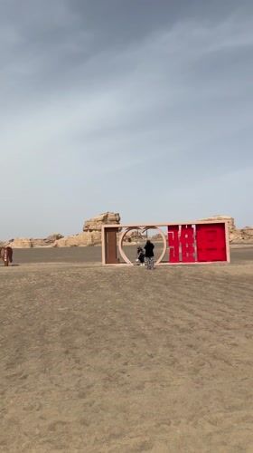 Two visitors approach decorative sign in Dunhuang desert