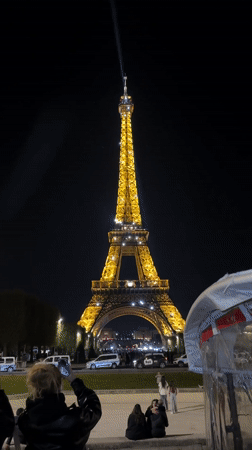 Eiffel Tower glows yellow as tourists gather for photos