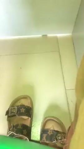 A person standing in a bathroom wearing Louis Vuitton sandals pans the camera around a white tiled room, showing a desk with books and boxes.