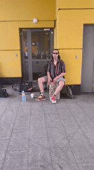 Street musician performs cajon drum outside yellow building
