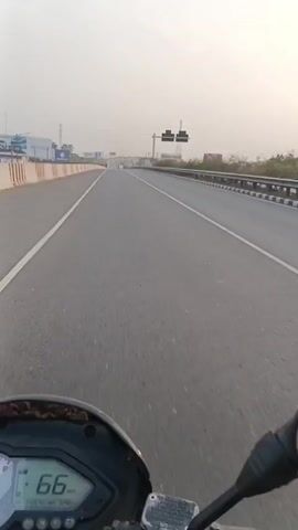 The video shows a first-person perspective of someone riding a motorcycle on a highway. The road is mostly empty with a few vehicles in the distance. There are billboards on the side of the road advertising brands such as Suzuki, Hyundai, and Seven Rings Cement. The sky is overcast, and there are power lines and pylons visible in the background. The motorcycle is moving forward on the asphalt highway. The video is shaky.