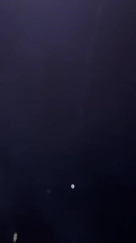 The video shows a dark, blurry landscape with a few faint lights visible in the distance. The lights appear as small, out-of-focus circles or streaks. There are no discernible people or objects in the foreground. The overall impression is of a night scene, possibly with fog or haze obscuring visibility.