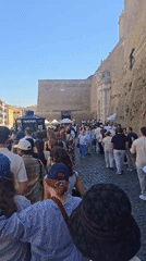 Crowds queue along Rome's cobblestone streets on a clear morning