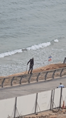 Person with long object walks fence railing near Tel Aviv beach