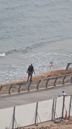 Person with long object walks fence railing near Tel Aviv beach