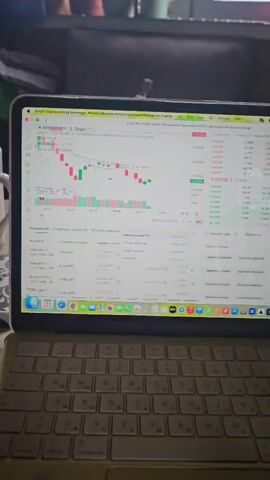 This video shows a close-up of a laptop screen displaying a cryptocurrency trading platform, likely BingX. The screen shows a trading chart with candlestick patterns in red and green, indicating price fluctuations. Below the chart, there is a section displaying "Positions" with details about open orders, including "CARVUSDT," "SAFECRYPTO," and "RESOLVUSDT." The trading platform interface includes various menus and buttons related to trading, such as "Open Orders," "Order History," and "Realized P/L." On the right side of the screen, a list of buy and sell orders is visible, showing prices and quantities of "USDT" and other cryptocurrencies.

The video captures the laptop in a home setting, possibly a desk, as suggested by the keyboard and a white mug visible on the left side of the frame. The lighting suggests it could be daytime or evening, but the specific time of day is not definitively clear. The overall scene is focused on the activity of cryptocurrency trading, with no people visible. The visible text includes currency pairs like "RESOLVUSDT," "USDT," "BTCUSDT," "ETHUSDT," and "SOLUSDT," along with timestamps and trading-related terms in Russian, such as "Открытые ордера" (Open Orders) and "История ордеров" (Order History). The timestamp on the screen reads "20:37:32 UTC+3."