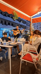 Street musician serenades family at outdoor restaurant in Spain