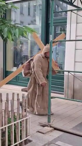 Robed figure carries wooden cross through Vienna city center