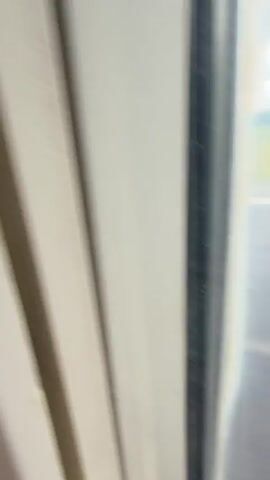 The video shows a view from an airplane window during a landing. The wing of the plane is visible, along with the runway and a grassy area beyond. The window is wet, obscuring the view. The plane is moving, as indicated by the blurring of the ground. The words "RYANAI" are partially visible on the wing. The sky is overcast.