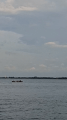 Kids swimming and fishing boats along Lhokseumawe's overcast shoreline