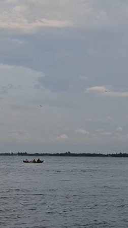 Kids swimming and fishing boats along Lhokseumawe's overcast shoreline