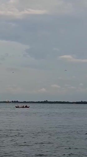 Kids swimming and fishing boats along Lhokseumawe's overcast shoreline
