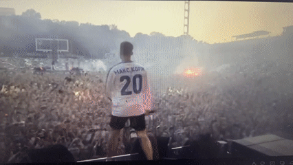 Stadium concert performer in white jersey faces crowd